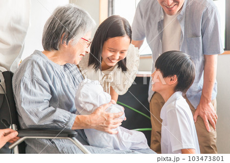 赤ちゃんと対面する車椅子に乗った高齢者女性と子供達・家族 赤ちゃんと対面する車椅子に乗った高齢者女性と子供達・家族 103473801