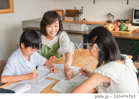 家で夏休みの宿題を手伝う母親と勉強する子供達 103474763