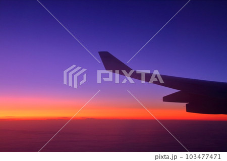 飛行機の機窓から翼のシルエットと夜明け前の朝焼け空 飛行機の機窓から翼のシルエットと夜明け前の朝焼け空 103477471