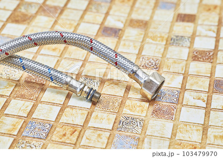 Plumbing. Flexible metal stainless steel faucet hoses on light brown pvc panel Plumbing. Flexible metal stainless steel faucet hoses on light brown pvc panel 103479970