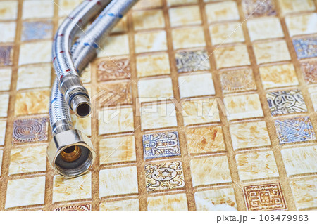 Plumbing. Flexible metal stainless steel faucet hoses on light brown pvc panel 103479983