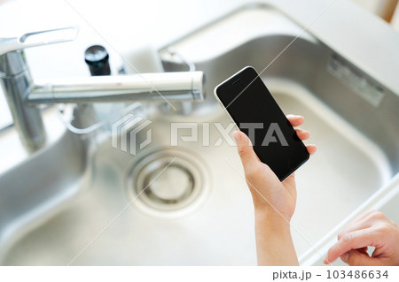キッチンシンクとスマートフォンを持つ手元写真 103486634