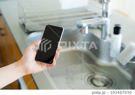 キッチンシンクとスマートフォンを持つ手元写真 103487030
