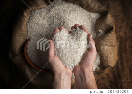 Human hands in shape of heart holding handful of rice over burlap sack 103489208