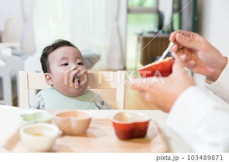 パパに離乳食を食べさせてもらいたくて口を開けて待っている生後8か月の赤ちゃん パパに離乳食を食べさせてもらいたくて口を開けて待っている生後8か月の赤ちゃん 103489871