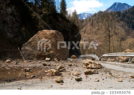A huge rock fell from the mountains onto the road, destroying the asphalt and blocking half of the roadway. A huge rock fell from the mountains onto the road, destroying the asphalt and blocking half of the roadway. 103493076