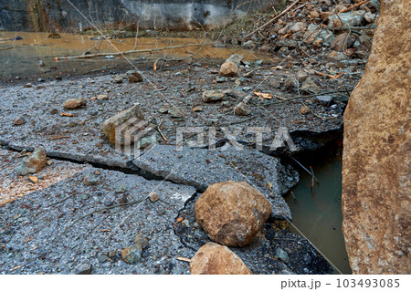 A huge rock fell from the mountains onto the road, destroying the asphalt and blocking half of the roadway. 103493085