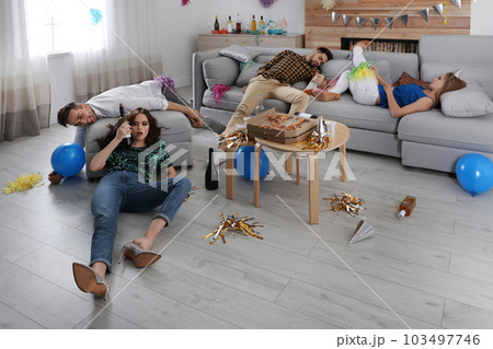 Drunk friends suffering from hangover in messy room after party 103497746