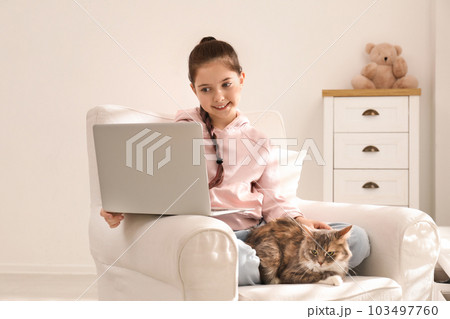 Cute little girl with laptop and cat in armchair at home. First pet 103497760