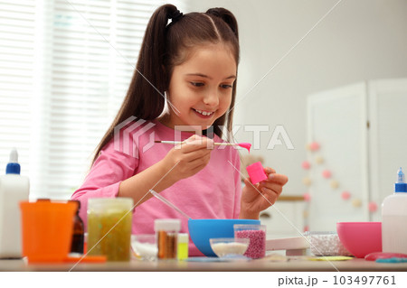 Cute little girl making homemade slime toy at table indoors 103497761