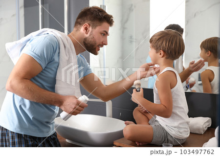 Dad applying shaving foam onto son's face in bathroom 103497762