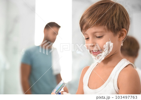 Happy little boy with shaving foam on face in bathroom, space for text. Dad and son having fun 103497763