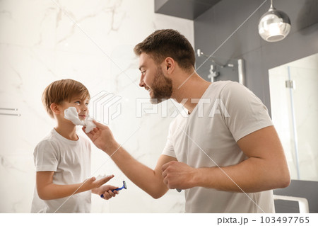 Dad applying shaving foam onto son's face in bathroom 103497765