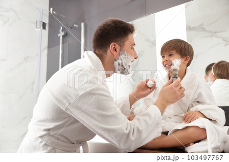 Dad applying shaving foam onto son's face in bathroom 103497767