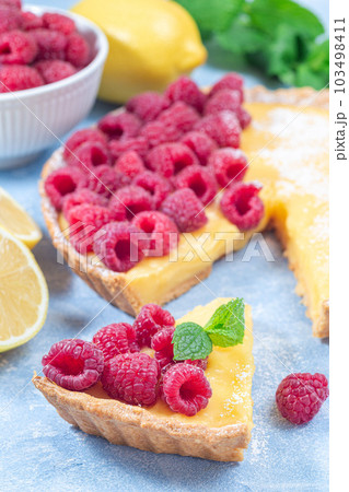 Piece of lemon tart, garnished with fresh raspberry, icing sugar, mint, vertical Piece of lemon tart, garnished with fresh raspberry, icing sugar, mint, vertical 103498411