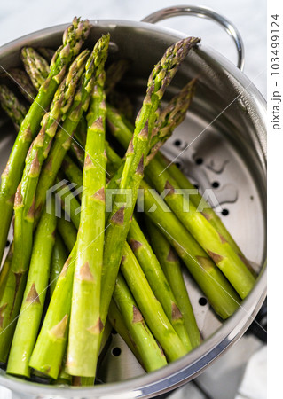Steaming fresh asparagus in stainless steel steaming pot. 103499124