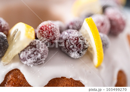 Lemon cranberry bundt cake decorated with sugar cranberries and lemon wedges on a cake stand. Lemon cranberry bundt cake decorated with sugar cranberries and lemon wedges on a cake stand. 103499270
