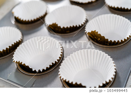 Scooping cupcake batter with dough scoop into a baking cupcake pan with liners to bake dulce de leche cupcakes. 103499445