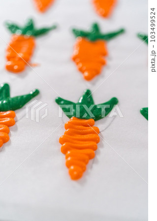 Piping melted chocolate from a piping bag over the parchment paper to make chocolate carrot cake toppers. Piping melted chocolate from a piping bag over the parchment paper to make chocolate carrot cake toppers. 103499524