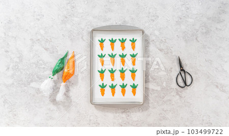 Flat lay. Piping melted chocolate from a piping bag over the parchment paper to make chocolate carrot cake toppers. 103499722