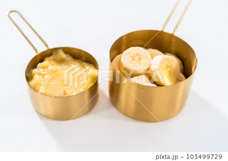 Mashed overripe bananas and sliced riped bananas in metal measuring cups. 103499729