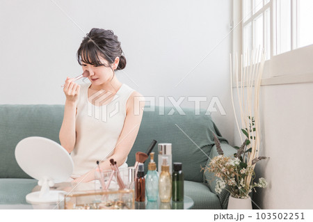 家でメイクブラシを使って鼻筋のハイライト・ハイライターなどのメイク・化粧する女性 103502251