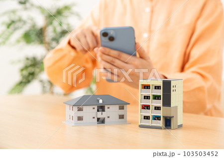 スマホを操作するシニア女性と住宅 103503452