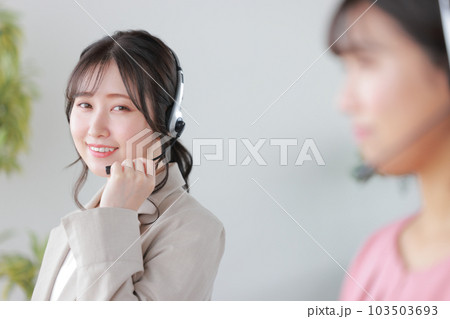 ヘッドセットを支え応対する女性オペレーター1_オフィスカジュアル 103503693