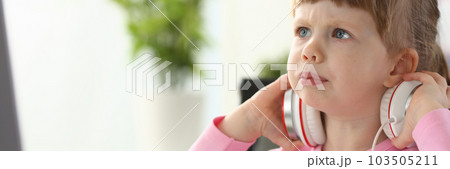 Portrait of a little beautiful child girl carefully looks at monitor in headphones Portrait of a little beautiful child girl carefully looks at monitor in headphones 103505211