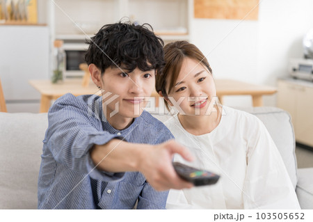 ソファーに座ってリモコンを手に持ってテレビ鑑賞している夫婦 103505652
