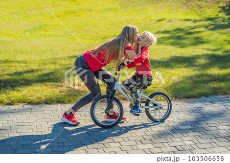 Young mother teaching her son how to ride a bicycle in the park 103506658