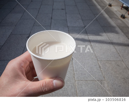 【日本】東京葛飾区、柴又の帝釈天通りで売られる甘酒の入った紙コップを持つ手と石畳 103506816