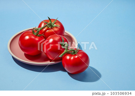 Background for the presentation of cosmetic products with tomato ingredient. Some ripe fresh tomatoes decorated on a round plate on a blue background. Blank space for design Background for the presentation of cosmetic products with tomato ingredient. Some ripe fresh tomatoes decorated on a round plate on a blue background. Blank space for design 103506934