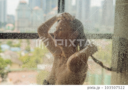 Beautiful woman in the shower behind glass with drops on the background of a window with a panoramic view of the city Beautiful woman in the shower behind glass with drops on the background of a window with a panoramic view of the city 103507522