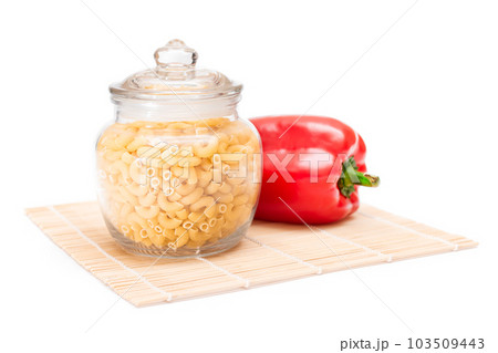 Uncooked Chifferi Rigati Pasta in Glass Jar and Red Bell Pepper on Bamboo Mat Isolated Uncooked Chifferi Rigati Pasta in Glass Jar and Red Bell Pepper on Bamboo Mat Isolated 103509443