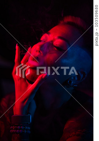 Sensual portrait of asian woman with short haircut smoking in neon light.  103509680