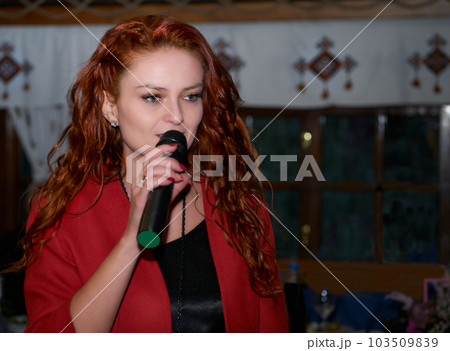 Red haired woman event host speaks with a microphone in a dark room 103509839