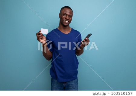 30 year old American guy in a casual t-shirt shows a mock-up of a money card and a phone 103510157