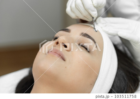 The beautician presents a luxurious procedure for deep cleansing of the skin in a beauty clinic, where a young woman, close-up, enjoys calm and healing moments of skin care. The beautician presents a luxurious procedure for deep cleansing of the skin in a beauty clinic, where a young woman, close-up, enjoys calm and healing moments of skin care. 103511758