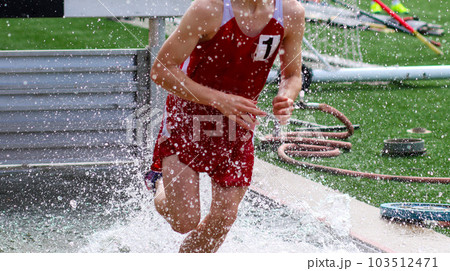 Young runner splashing in the water of the Steeplechase during a track race Young runner splashing in the water of the Steeplechase during a track race 103512471
