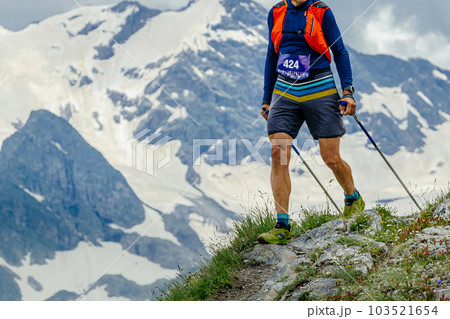 man athlete walk skyrunning marathon trail race in background snowy mountain, trekking poles in hands man athlete walk skyrunning marathon trail race in background snowy mountain, trekking poles in hands 103521654