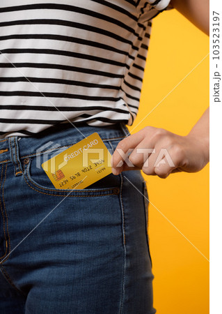 hand of person woman holding plastic credit card out of the pocket blue jean plants isolated on yellow studio background. online shopping payment, bill, currency, pay money, finance concept. 103523197