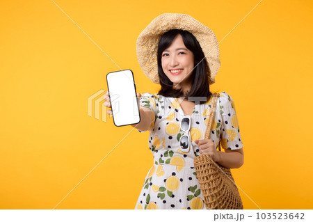 Portrait happy young asian woman with springtime dress fashion showing blank mobile application display screen for advertisement isolated on yellow background. Smartphone app technology concept. 103523642