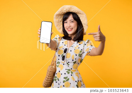Portrait happy young asian woman with springtime dress fashion showing blank mobile application display screen for advertisement isolated on yellow background. Smartphone app technology concept. Portrait happy young asian woman with springtime dress fashion showing blank mobile application display screen for advertisement isolated on yellow background. Smartphone app technology concept. 103523643
