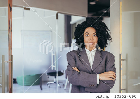 Portrait of serious female boss inside business company office, businesswoman crossed arms looking concentrated at camera, wearing shirt, satisfied and successful woman with curly hair. Portrait of serious female boss inside business company office, businesswoman crossed arms looking concentrated at camera, wearing shirt, satisfied and successful woman with curly hair. 103524690