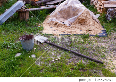 Shovel and bucket of sand on a construction site in the village. Construction site. Building tools. Shovel and bucket of sand on a construction site in the village. Construction site. Building tools. 103524731