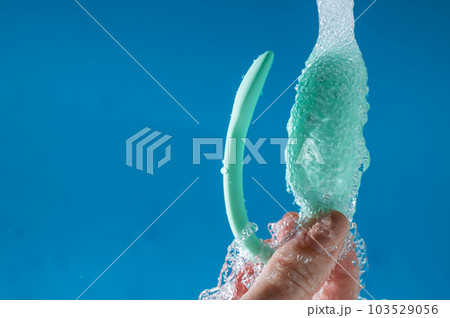 A woman washes a vibrator under running water on a blue background. Women's Health Kegel Trainer.  103529056