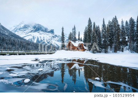 Frozen Emerald Lake with wooden lodge in pine forest on winter Frozen Emerald Lake with wooden lodge in pine forest on winter 103529954