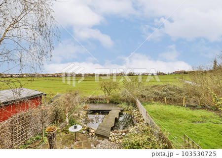 an old red shed in the middle of a green field, with trees and grass on either side there is a blue sky 103530725