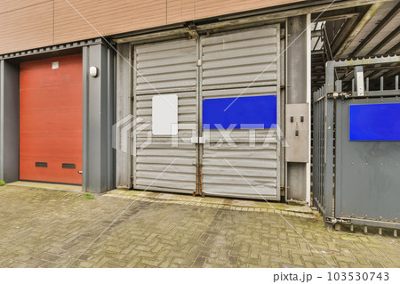 an industrial building with red and blue doors on either side of the building there is a brick sidewalk in front of it an industrial building with red and blue doors on either side of the building there is a brick sidewalk in front of it 103530743